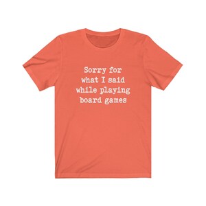 May include: Coral coloured t-shirt with the text "Sorry for what I said while playing board games" printed in white.