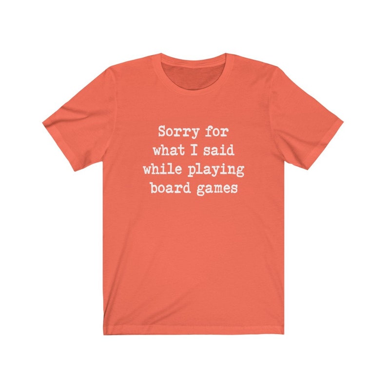 May include: Coral coloured t-shirt with the text "Sorry for what I said while playing board games" printed in white.