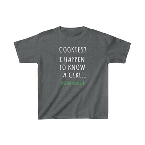 May include: A dark heather grey t-shirt with white text that reads "COOKIES? I HAPPEN TO KNOW A GIRL... #SCOUTBROTHER".