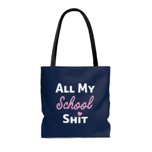 Op de afbeelding: Een donkerblauwe tote bag met witte tekst die "All My School Shit" zegt met een roze hart. Het woord "School" staat in roze cursief.
