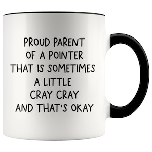 May include: White ceramic coffee mug with a black rim and handle. The mug has black text that reads "Proud parent of a pointer that is sometimes a little cray cray and that's okay."