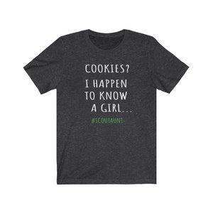 May include: A dark heather grey t-shirt with white text that reads "COOKIES? I HAPPEN TO KNOW A GIRL... #SCOUTAUNT"