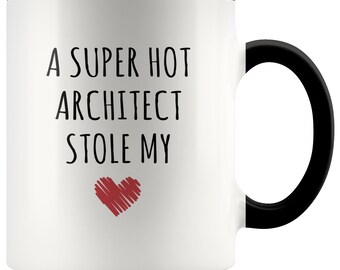 May include: White ceramic coffee mug with a black rim and handle. The mug has black text that reads "A super hot architect stole my" with a red heart below the text.