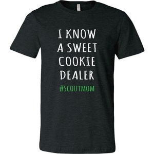 May include: A dark heather grey t-shirt with white text that reads "I know a sweet cookie dealer #scoutmom".