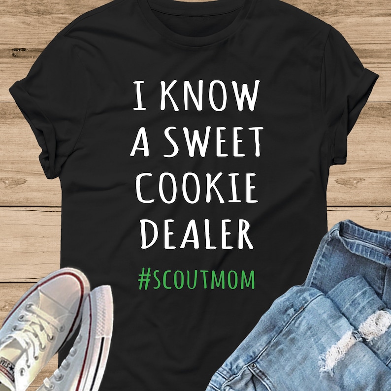 May include: Black t-shirt with white text that reads "I know a sweet cookie dealer #scoutmom" in green text.