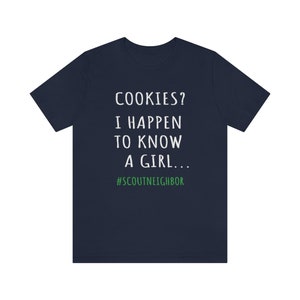 May include: Navy blue t-shirt with white text that reads "COOKIES? I HAPPEN TO KNOW A GIRL... #SCOUTNEIGHBOR".