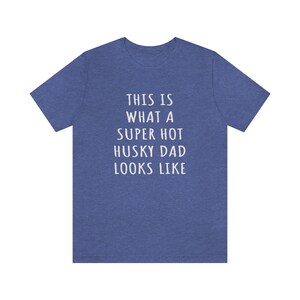 May include: A blue heather t-shirt with the text "This is what a super hot husky dad looks like" printed in white.