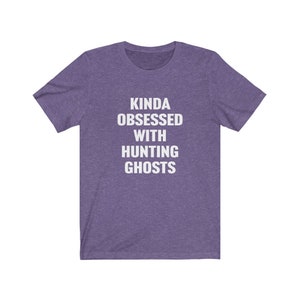 May include: Purple short-sleeved t-shirt with white text that reads "Kinda obsessed with hunting ghosts".