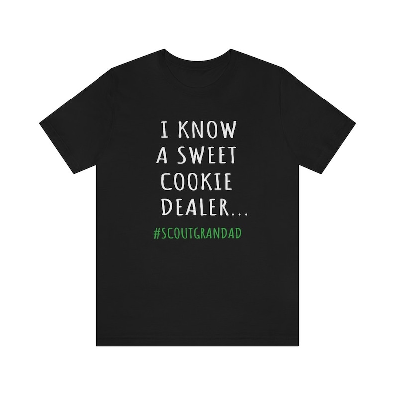 Op de afbeelding: Zwart T-shirt met witte tekst die "I know a sweet cookie dealer... #ScoutGrandad" luidt in een handschrift-stijl. De hashtag is groen.