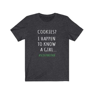 May include: Dark heather grey t-shirt with white text that reads "COOKIES? I HAPPEN TO KNOW A GIRL... #SCOUTBROTHER".