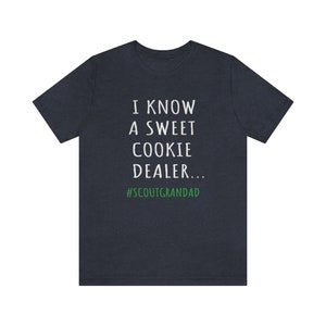 Op de afbeelding: Een donkerblauw t-shirt met witte tekst die "I know a sweet cookie dealer... #ScoutGrandad" in wit met de hashtag in groen zegt.