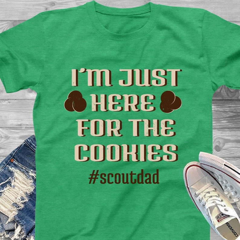 May include: Green t-shirt with the text "I'm just here for the cookies #scoutdad" in brown and white lettering.