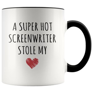 May include: White ceramic coffee mug with a black rim and handle. The mug has black text that reads "A super hot screenwriter stole my" with a red heart underneath.
