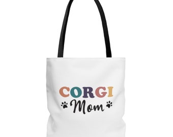 May include: White canvas tote bag with black handles. The bag has a colorful graphic that says "CORGI Mom" with paw prints on either side of the word "Mom".