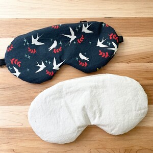 May include: A black sleep mask with a white bird and leaf pattern on one side and a plain white side on the other.