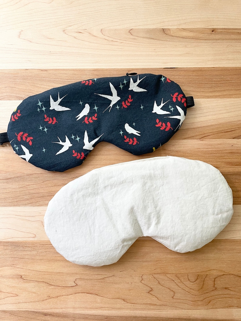 May include: A black sleep mask with a white bird and leaf pattern on one side and a plain white side on the other.