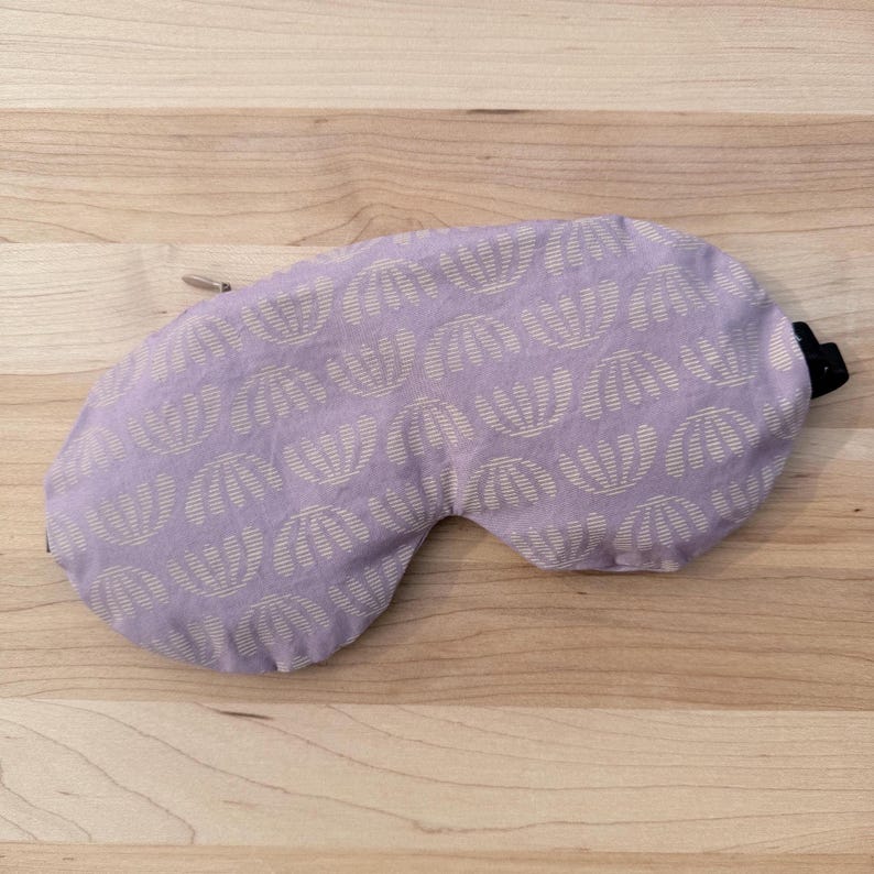 Puede incluir: Una m&aacute;scara para los ojos de color lavanda con un patr&oacute;n repetido de conchas blancas. La m&aacute;scara tiene una correa el&aacute;stica negra y un ajustador de metal plateado. Dise&ntilde;ada para bloquear la luz para dormir o relajarse.