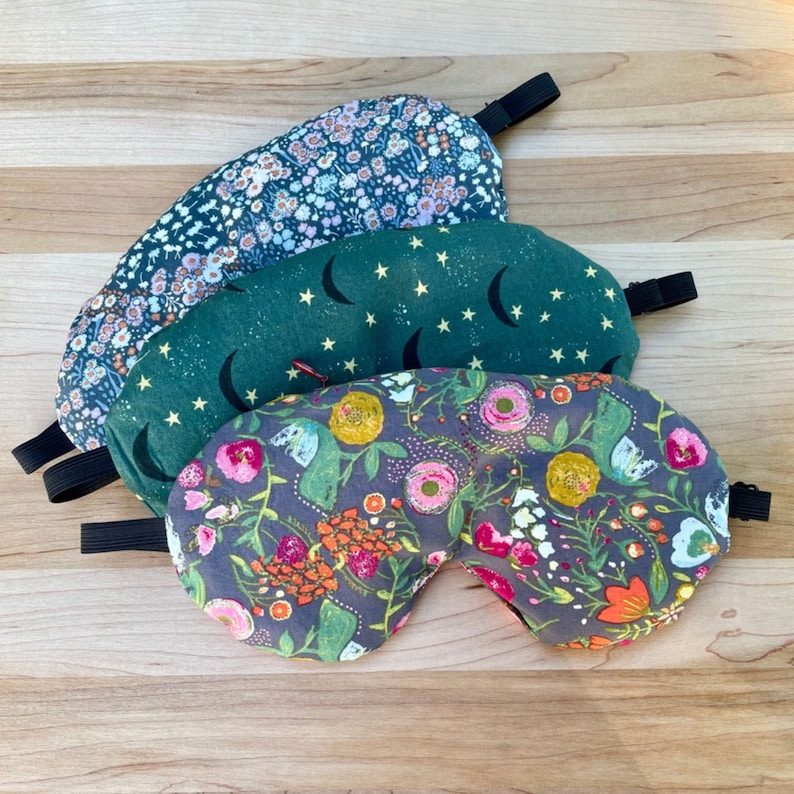 Puede incluir: Se muestran cuatro antifaces para dormir con bandas el&aacute;sticas. La m&aacute;scara superior tiene un estampado floral azul. La segunda m&aacute;scara es verde con lunas crecientes y estrellas. La tercera m&aacute;scara tiene un estampado floral con flores rosas y amarillas. La m&aacute;scara inferior tiene un estampado floral.