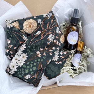 Pode incluir: Uma caixa de presente contendo uma almofada para os olhos com estampa floral verde escuro, um frasco de spray de vidro marrom e um frasco roll-on de vidro marrom. As garrafas têm rótulos "Sleep". A caixa é forrada com papel de seda branco.