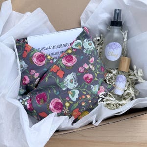 Pode incluir: Uma caixa de presente contendo uma compressa para o pescoço floral cinza, um frasco de spray e um frasco roll-on. A compressa tem um padrão floral com flores rosa, laranja e brancas. Os frascos têm rótulos "Sleep".