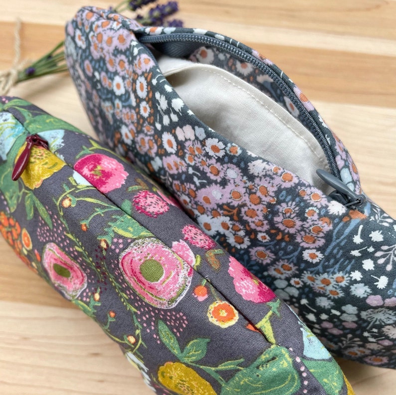 May include: Two zippered pouches with floral patterns. The pouch on the left has a red zipper and a floral pattern with pink, yellow, and green flowers. The pouch on the right has a gray zipper and a floral pattern with pink, white, and blue flowers.