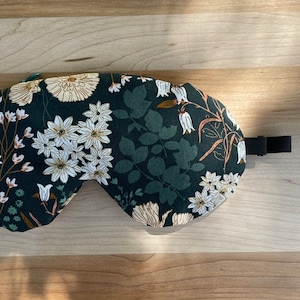 Puede incluir: Una m&aacute;scara para dormir verde oscuro con un estampado floral con flores blancas y beige y hojas verdes. La m&aacute;scara tiene una correa el&aacute;stica negra. Dise&ntilde;ada para bloquear la luz y mejorar el sue&ntilde;o.