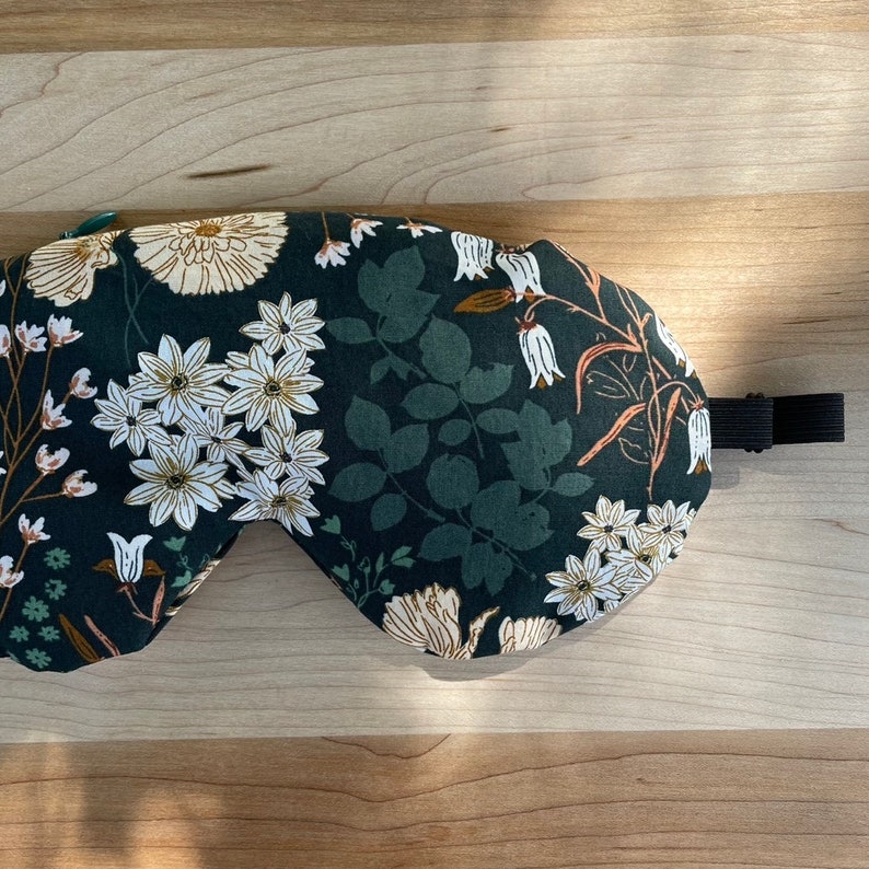 Puede incluir: Una m&aacute;scara para dormir verde oscuro con un estampado floral con flores blancas y beige y hojas verdes. La m&aacute;scara tiene una correa el&aacute;stica negra. Dise&ntilde;ada para bloquear la luz y mejorar el sue&ntilde;o.