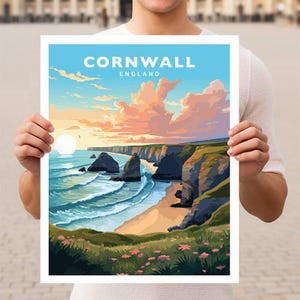 May include: A vintage travel poster featuring a scenic view of Cornwall, England. The poster depicts a rocky coastline with a sandy beach, turquoise water, and a bright pink and orange sky. The text "Cornwall, England" is printed at the top of the poster.