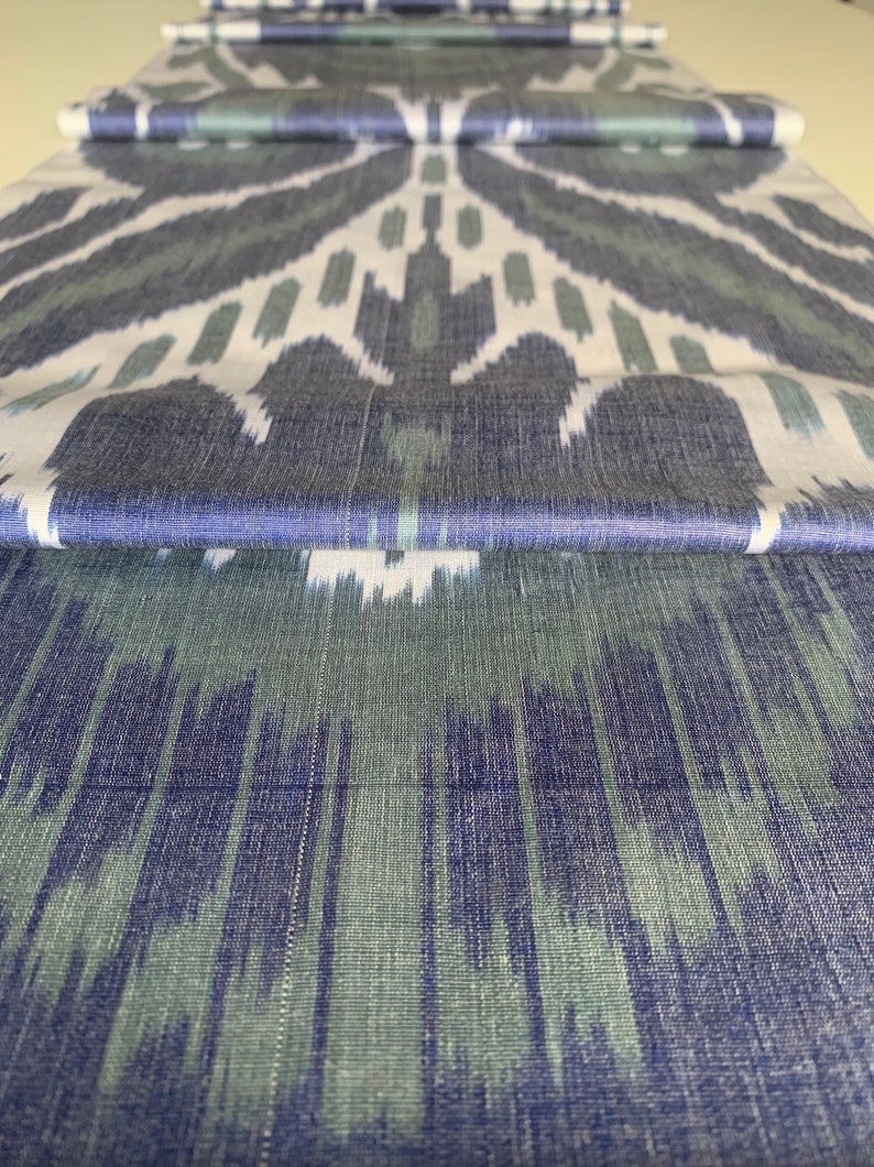 Puede incluir: Tela ikat azul y verde sobre fondo blanco. La tela tiene una textura tejida y un patr&oacute;n repetitivo.