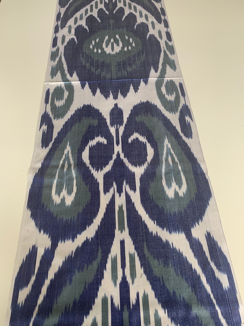 Puede incluir: Una tela blanca con un patr&oacute;n ikat azul y verde. El patr&oacute;n es un dise&ntilde;o tradicional con un motivo repetitivo de flores y hojas estilizadas.