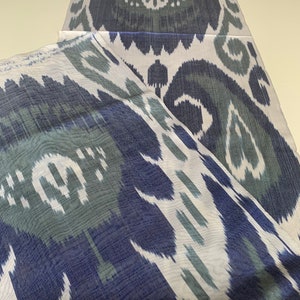 Puede incluir: Dos piezas de tela blanca con un patr&oacute;n ikat azul y verde. La tela est&aacute; doblada por la mitad y el patr&oacute;n es visible en ambos lados.