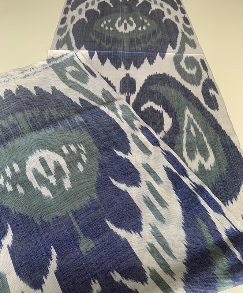 Puede incluir: Dos piezas de tela blanca con un patr&oacute;n ikat azul y verde. La tela est&aacute; doblada por la mitad y el patr&oacute;n es visible en ambos lados.
