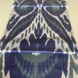 Puede incluir: Una tela blanca con un patr&oacute;n ikat azul y verde. La tela est&aacute; doblada en tres partes, mostrando el patr&oacute;n que se repite.