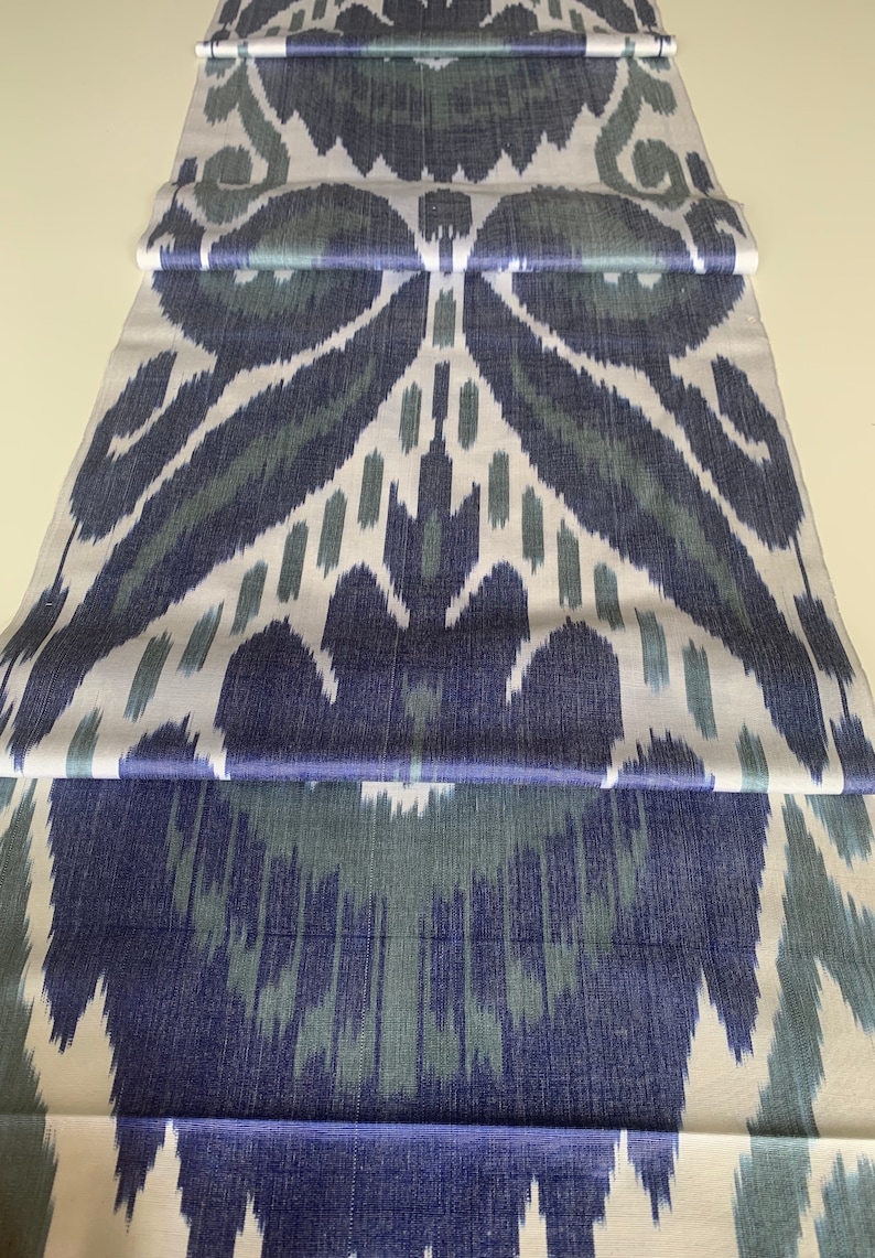 Puede incluir: Una tela blanca con un patr&oacute;n ikat azul y verde. La tela est&aacute; doblada en tres partes, mostrando el patr&oacute;n que se repite.