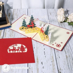 Biglietto di Natale pop-up 3D con renna dorata nella foresta invernale
