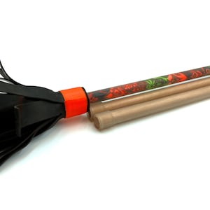 Può includere: Una scopa di gomma nera con un manico arancione attaccato a un'asta di legno. L'asta di legno è decorata con un motivo colorato.