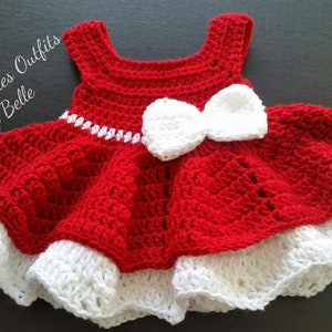 Pode incluir: Um vestido de beb&eacute; de crochet vermelho com um la&ccedil;o de crochet branco e uma bainha de crochet branco. O vestido &eacute; feito por Crochet Cuties Outfits by Belle.