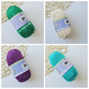 May include: Four skeins of yarn in various colors: green, cream, purple, and teal. Each skein has a label that reads "Cutie Outfits by Belle" and "Alpaca". The yarn is neatly wound and ready for crafting.