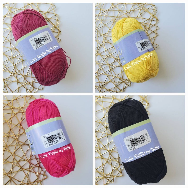 May include: Four skeins of yarn in various colors: burgundy, yellow, hot pink, and black. Each skein has a label with the text "EULALI" and "Cutie Outfits by Belle". The yarn is displayed on a gold-colored, woven surface.
