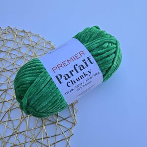 May include: A skein of green Premier Parfait Chunky yarn. The label reads "Premier Parfait Chunky" with details including 131 yards/120 m and 3.5 oz/100 g. The yarn is 100% polyester.