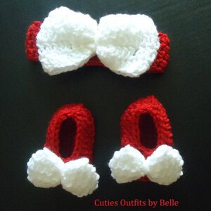 May include: A red and white crochet baby set, including a headband with a large bow and two booties with white bows. The text "Cuties Outfits by Belle" is visible at the bottom. The set is likely handmade.
