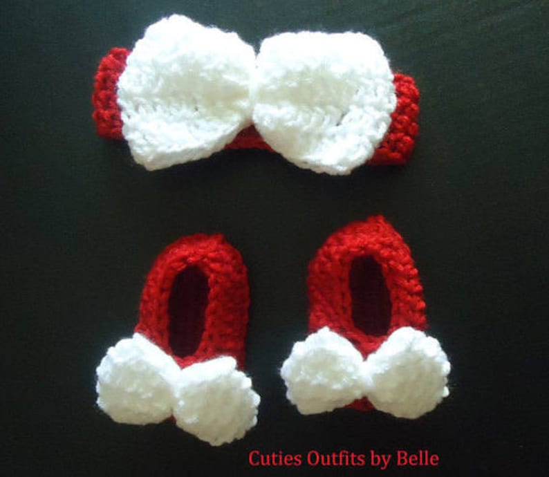 May include: A red and white crochet baby set, including a headband with a large bow and two booties with white bows. The text "Cuties Outfits by Belle" is visible at the bottom. The set is likely handmade.