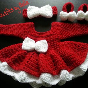 May include: A handmade red and white crochet baby outfit, including a dress with a bow, a headband, and booties. The dress features a white bow and trim. The text "Cuties outfits by Belle" is in the image.
