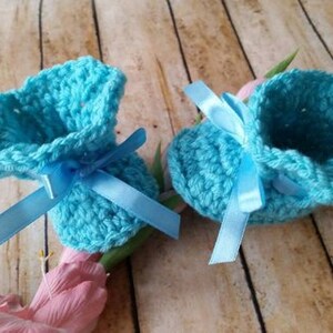 May include: A pair of light blue crocheted baby booties with blue satin ribbon bows.