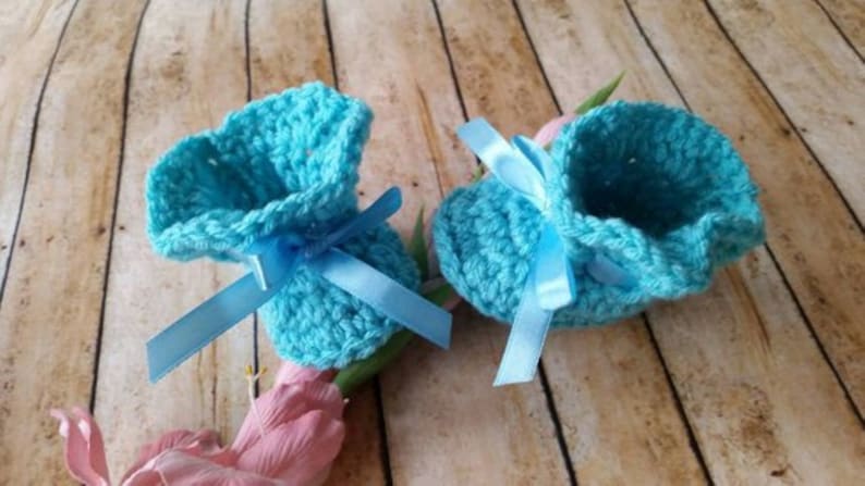 May include: A pair of light blue crocheted baby booties with blue satin ribbon bows.