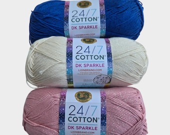 May include: Three skeins of DK Sparkle yarn in blue, cream, and pink. Each skein has a label that reads "24/7 Cotton DK Sparkle" and "Lionbrand.com". The yarn is tightly wound and appears soft, ideal for knitting or crochet projects.