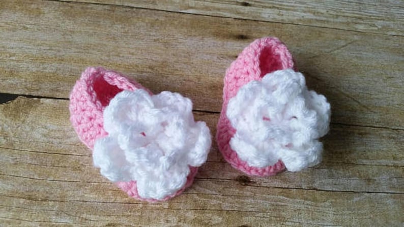 May include: A pair of pink crocheted baby shoes with white crocheted flowers on top.