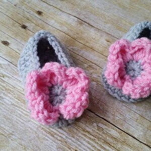 May include: A pair of gray crocheted baby booties with pink flower embellishments.