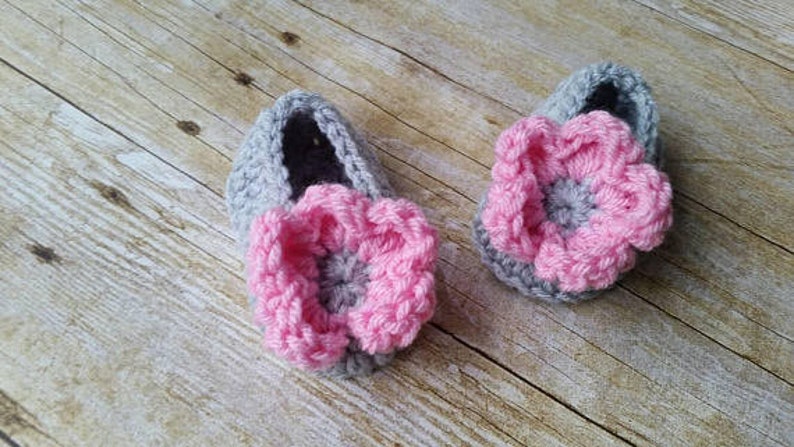 May include: A pair of gray crocheted baby booties with pink flower embellishments.