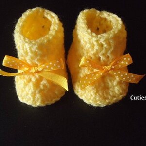 May include: A pair of yellow crocheted baby booties with yellow and white polka dot bows.